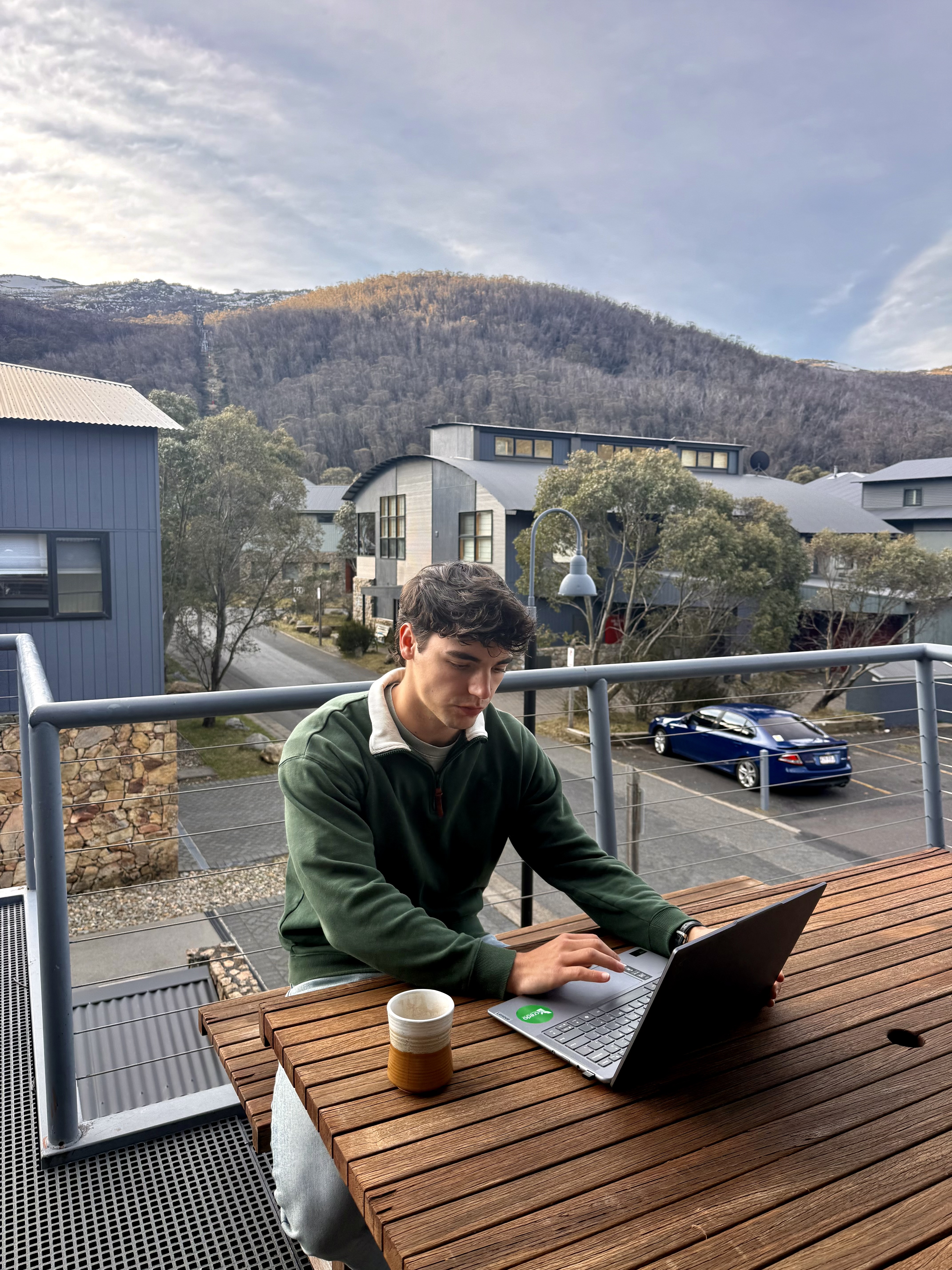 Henri working on his laptop at a table with mountains behind him